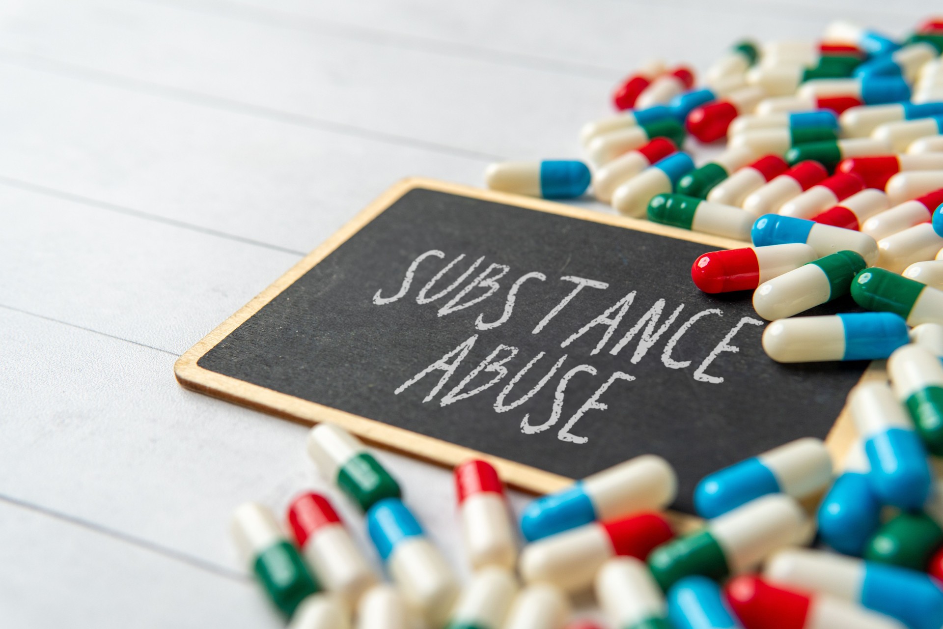 A chalkboard with the words SUBSTANCE ABUSE surrounded by scattered pills and capsules.